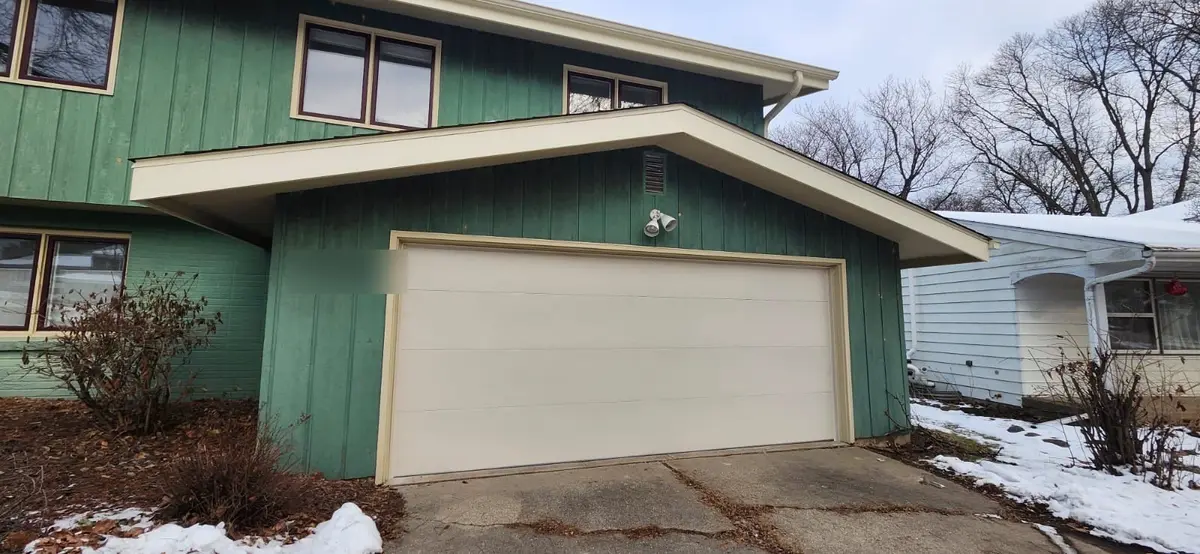 After: new cream flush garage door on the same green sided home