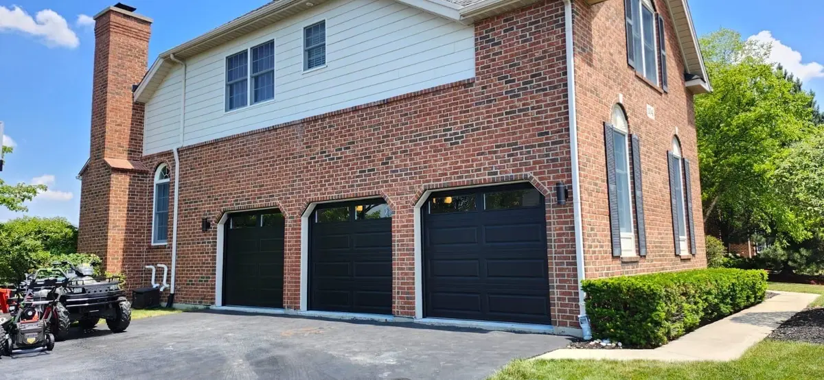 Three black garage doors on a two story brick home