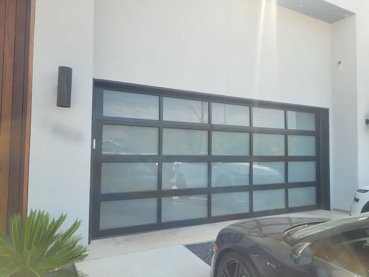 Black framed full view garage door with frosted glass on a white modern home