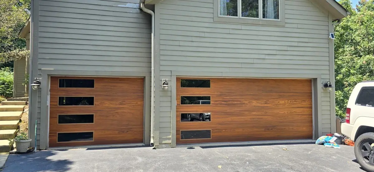 Pair of wood tone modern single garage doors on a grey sided home