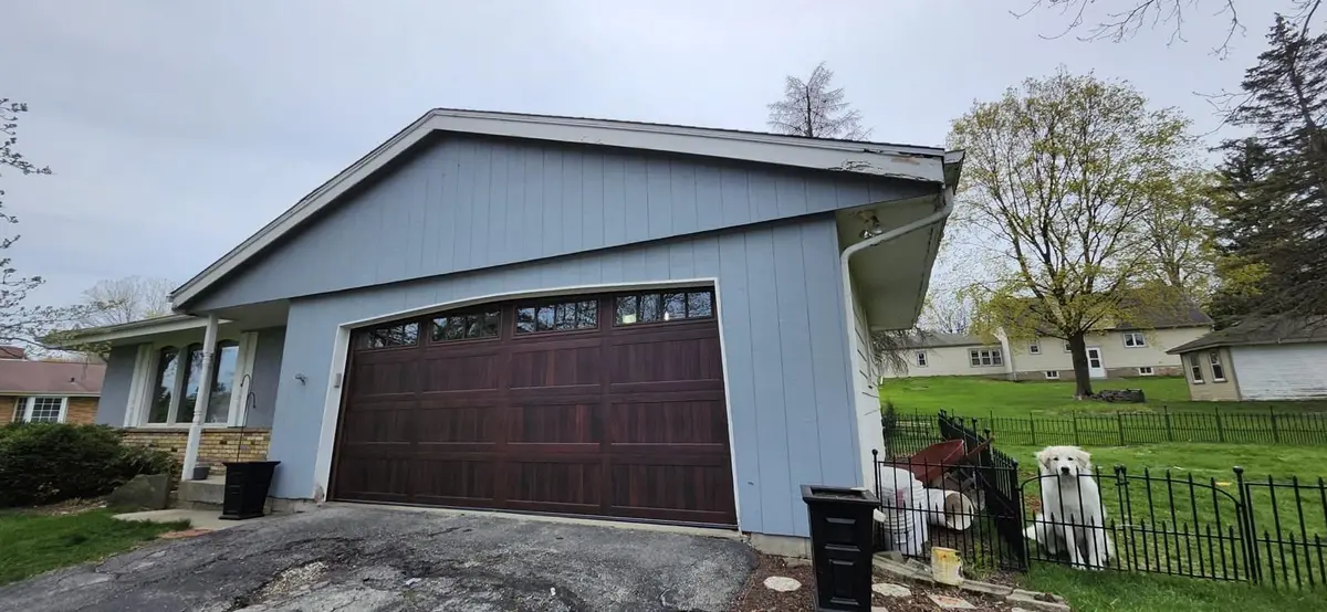 Wood tone garage door with windows on a blue sided garage