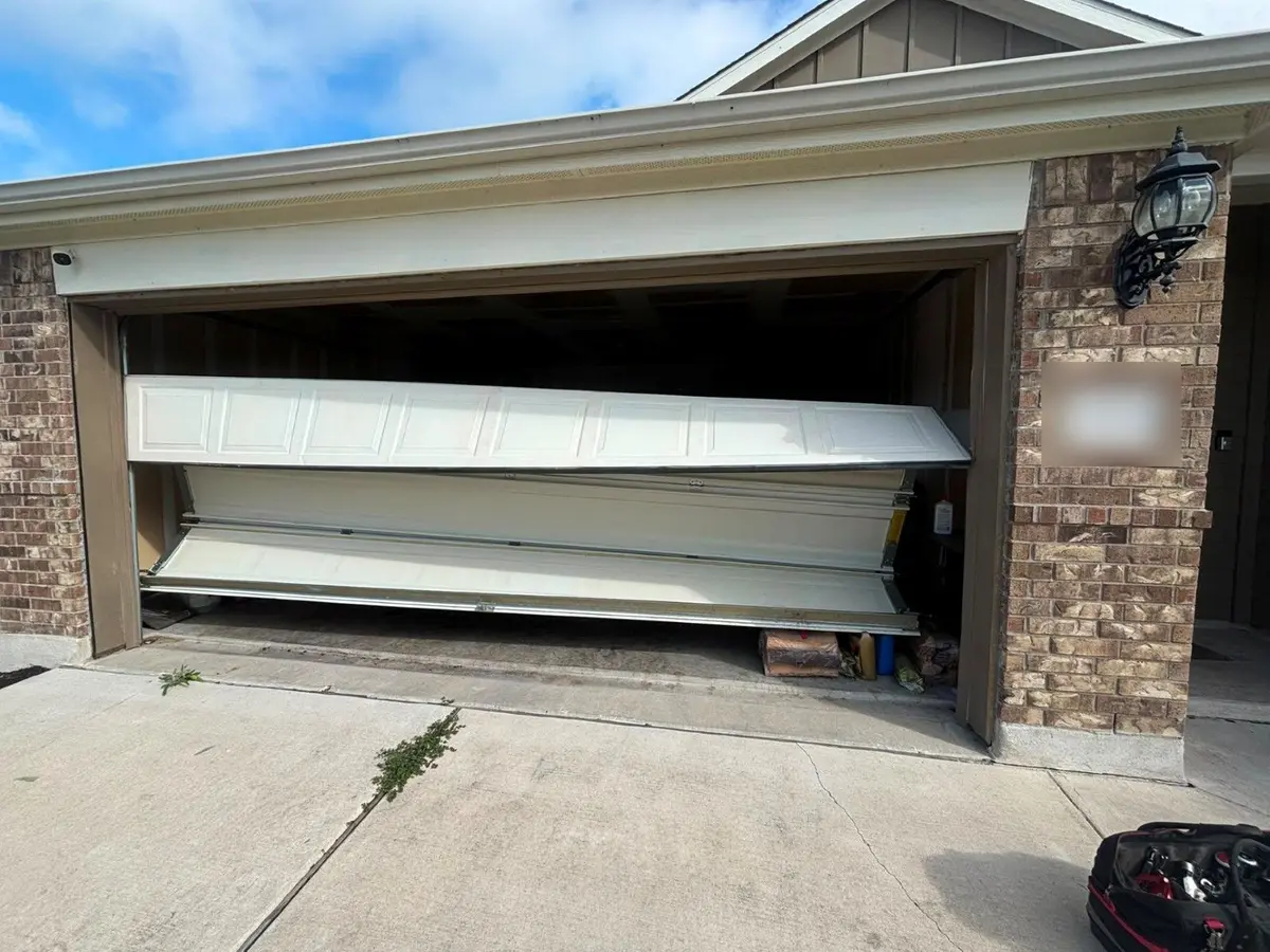 Garage door sections collapsed and hanging out of the opening on a brick home