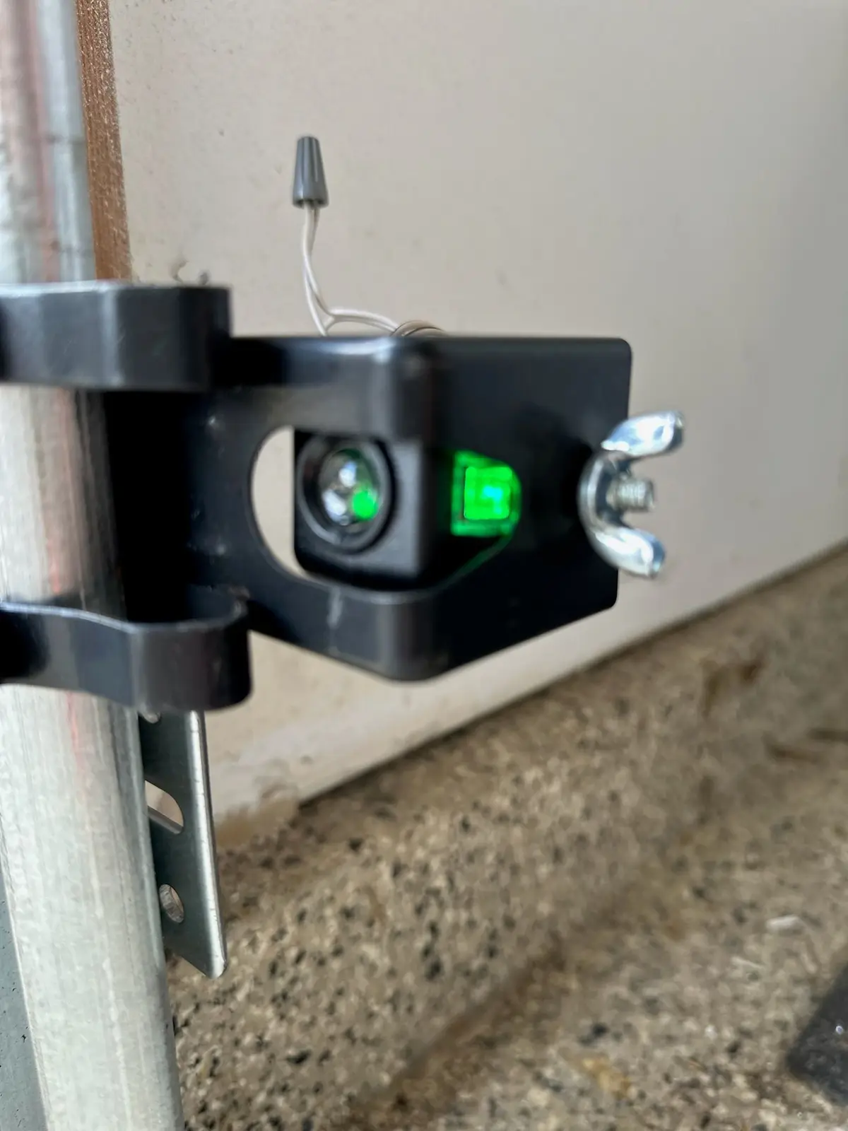 Garage door safety sensor on its bracket with a green indicator light on