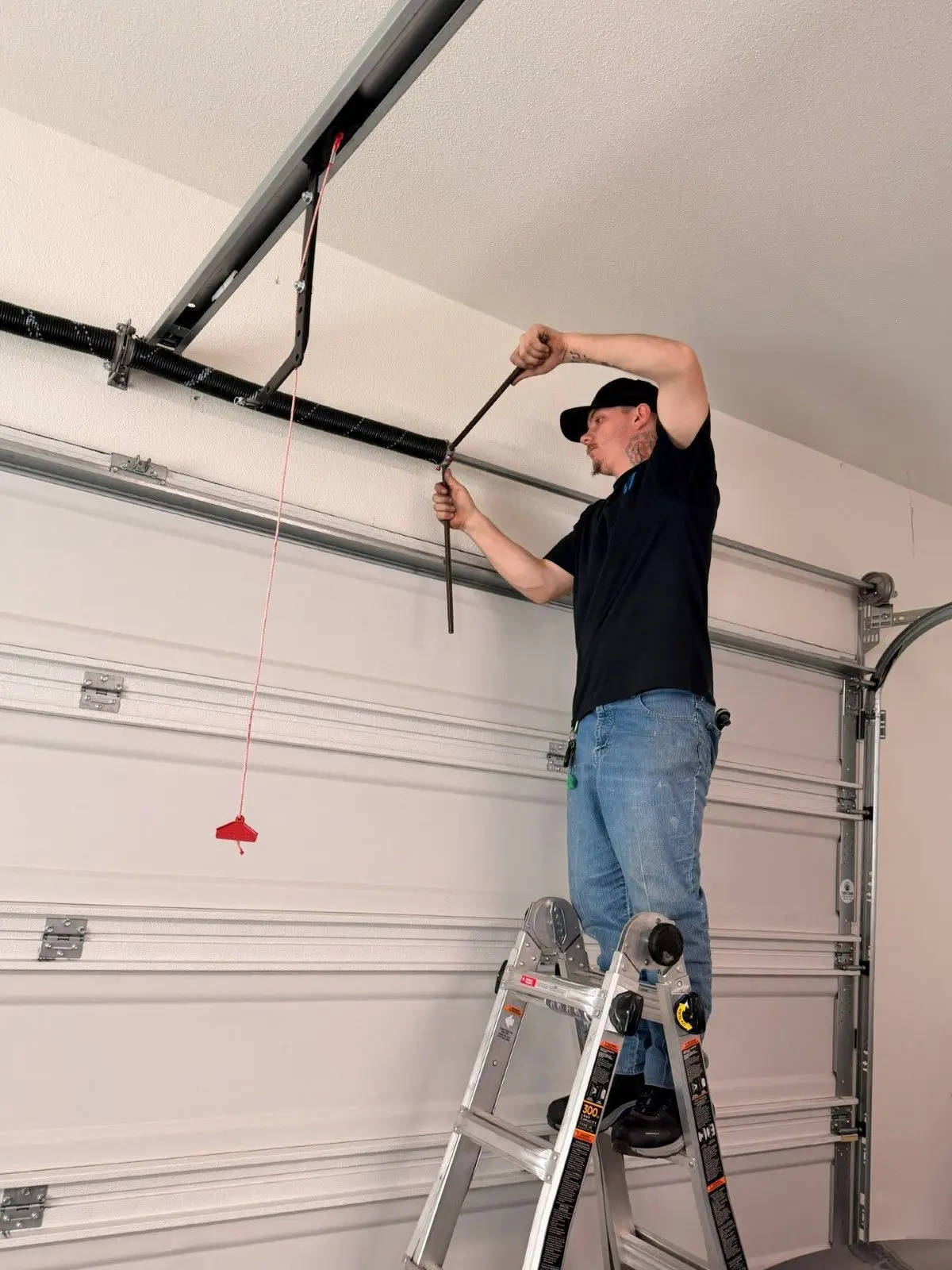 Tier One technician using winding bars to set a torsion spring above a garage door