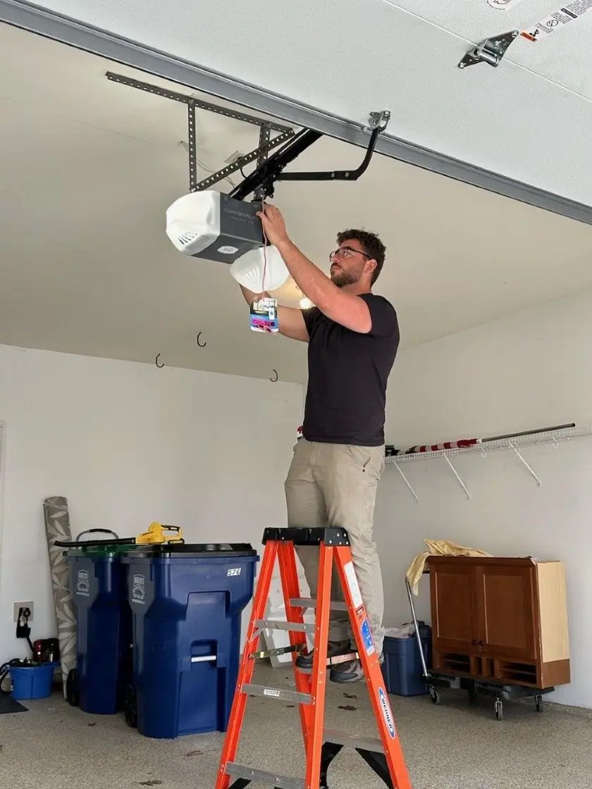 Technician on a ladder installing a garage door opener on a garage ceiling