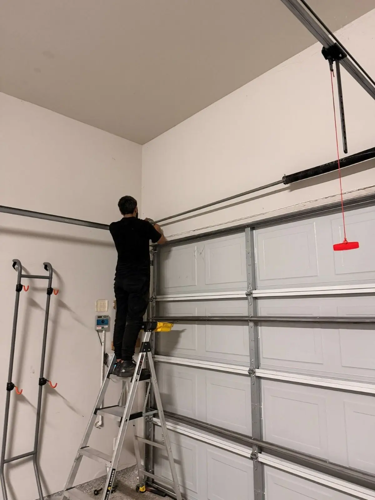 Tier One technician on a ladder fitting the spring assembly on a newly installed garage door