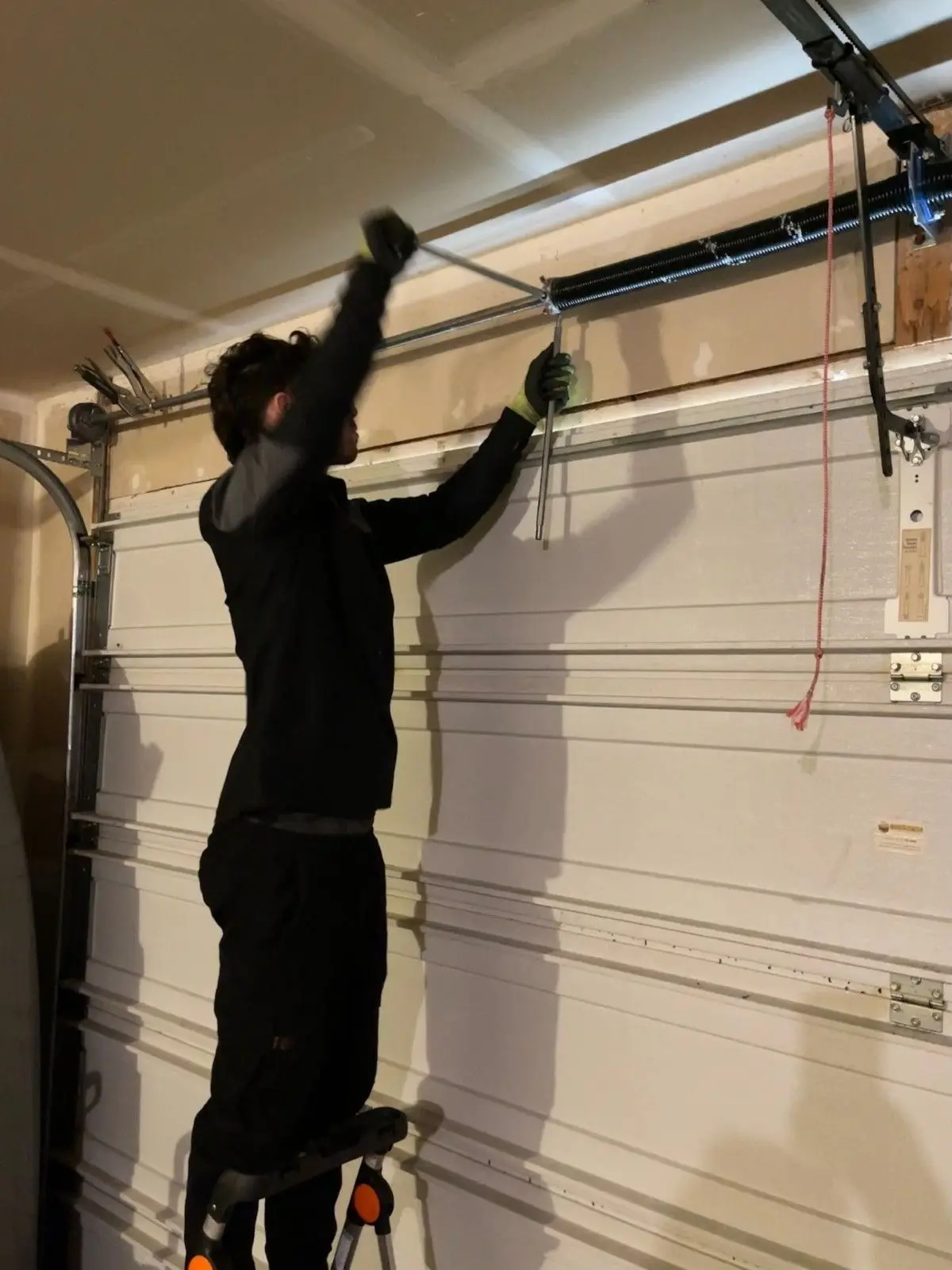 Tier One technician on a ladder working on the spring assembly above a garage door