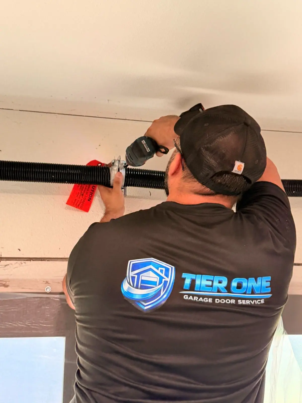 Tier One technician in a company shirt working on the spring assembly above a garage door